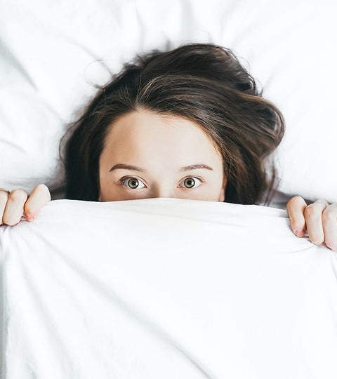 woman peeking out from under white duvet